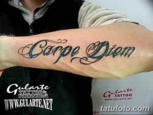 Фото татуировки с надписью 'Carpe Diem' на предплечье. Рисунок выполнен в бирюзовых и синих оттенках с черным контуром.