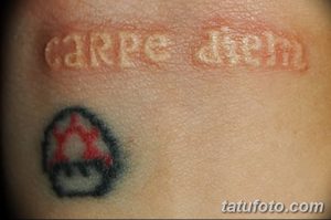 Фото татуировки 'Carpe Diem' с изображением символа на пальце. Черно-белая татуировка, простой шрифт, минималистичный дизайн.