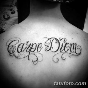 Фото тату надписи 'Carpe Diem' выполненной каллиграфическим шрифтом на спине мужчины. Черно-белая татуировка, четкие линии, классический стиль.