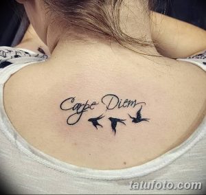 Фото тату: надпись 'Carpe Diem' и три летящие птицы на спине девушки. Минималистичный рисунок татуировки, выполненный в черном цвете.