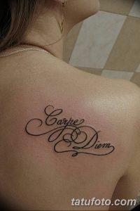 Фото тату: надпись 'Carpe Diem' изящным шрифтом на спине девушки. Минималистичный рисунок татуировки, выполненный в черном цвете.