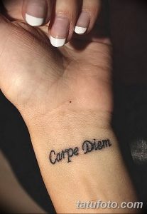 Фото тату: надпись 'Carpe Diem' изящным шрифтом на запястье девушки. Минималистичный рисунок татуировки, выполненный в черном цвете.