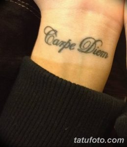 Фото тату: надпись 'Carpe Diem' на запястье. Минималистичный рисунок татуировки, выполненный в сером цвете.