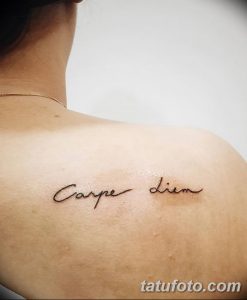 Фото тату: надпись 'Carpe Diem' изящным шрифтом на спине девушки. Минималистичный рисунок татуировки, выполненный в черном цвете.