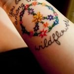 Фото тату: красочный цветочный венок с надписью 'You belong among the wildflowers' на женском предплечье.