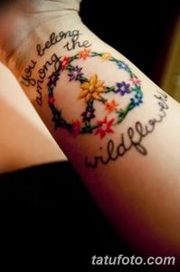 Фото тату: красочный цветочный венок с надписью 'You belong among the wildflowers' на женском предплечье.