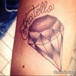 Фото тату бриллианта с надписью 'Fratello' на предплечье. Черно-серый рисунок татуировки, выполненный в реалистичном стиле, символизирует ценность братской любви.