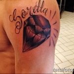 Фото татуировки на плече, изображающей большой бриллиант и надпись 'Lorella'. Выполнена в черно-серых тонах, с использованием теней. Символ роскоши и любви.