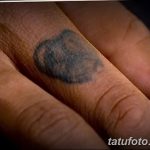 Фото тату на пальце: размытый, старый рисунок, трудно разобрать детали. Черный цвет, нечеткие контуры. Пример старой, выцветшей татуировки.