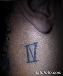 Фото минималистичной татуировки с римскими цифрами «IV» на коже за ухом. Четкий и лаконичный рисунок.
