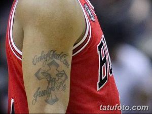 Фото тату креста с надписью 'Only God Can Judge Me' на плече мужчины в красной майке. Религиозная татуировка, черно-белое изображение.