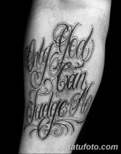 Черно-белое фото татуировки с надписью 'Only God can judge me' на руке мужчины. Изящный шрифт, декоративные элементы, сложный дизайн.