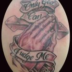Фото тату молящихся рук с надписью 'Only God Can Judge Me'. Черно-серая татуировка с детальной проработкой.