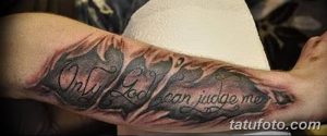 Фото тату надписи 'Only God Can Judge Me' на предплечье. Черно-серая татуировка, выполненная каллиграфическим шрифтом с эффектом трещин.
