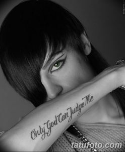 Фото тату надписи 'Only God Can Judge Me' на внутренней стороне предплечья девушки. Черно-белое изображение, каллиграфический шрифт.