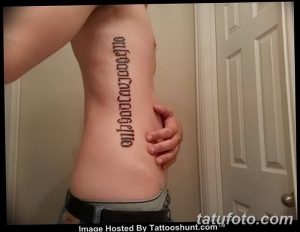 Фото тату надписи 'Only God Can Judge Me' на боку. Татуировка выполнена черным шрифтом, текст расположен вертикально.