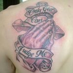 Фото тату на спине с изображением молящихся рук и надписи 'Only God Can Judge Me'. Татуировка выполнена в серо-розовых тонах.