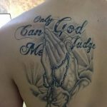 Фото тату на спине: молящиеся руки с четками и надписью 'Only God Can Judge Me', выполненное в реалистичном стиле с использованием серых оттенков.