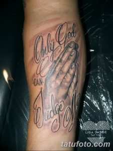 Фото тату на предплечье: сложенные в молитве руки с надписью 'Only God Can Judge Me', выполненное в реалистичном стиле с использованием черных и серых оттенков.