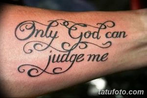 Фото тату надписи 'Only God Can Judge Me' на руке, выполненной в классическом стиле. Текст выполнен черным цветом, с четкими линиями и завитушками.