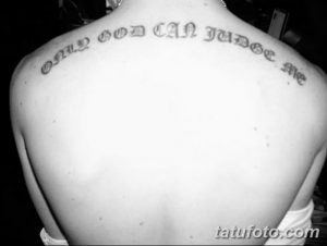 Фото тату надписи 'Only God Can Judge Me' на спине, выполненной в черно-белом цвете. Текст расположен вдоль позвоночника, выполнен в готическом шрифте.