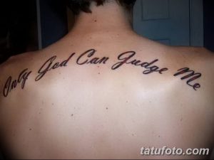 Фото тату надписи 'Only God Can Judge Me' на спине мужчины. Надпись выполнена в изящном шрифте с плавными линиями, черным цветом.
