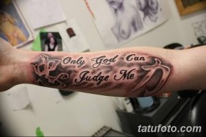 Фото татуировки на предплечье с надписью 'Only God Can Judge Me' и декоративными элементами. Черно-серый рисунок.