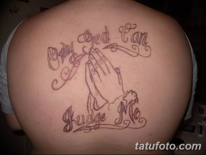 Фото тату молящихся рук с надписью 'Only God Can Judge Me' на спине. Черно-серый рисунок татуировки с религиозной символикой.