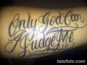 Фото тату с надписью 'Only God Can Judge Me', выполненной в каллиграфическом стиле на руке. Черно-серый рисунок татуировки с витиеватыми элементами.