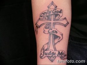 Фото тату креста с надписью 'Only God Can Judge Me' на предплечье. Черно-серый рисунок татуировки в стиле традиционной религиозной символики.