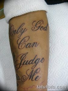 Фото тату надписи 'Only God can judge me' на мужской руке. Черно-серый рисунок татуировки выполнен каллиграфическим шрифтом с плавными линиями.