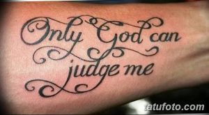 Фото тату надписи 'Only God can judge me' на мужском запястье. Черно-серый рисунок татуировки выполнен элегантным шрифтом с декоративными элементами.