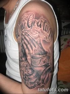Фото тату 'Only God can judge me' на мужском предплечье. Рисунок татуировки включает молящиеся руки, цепи и надпись, выполненные в реалистичном стиле.