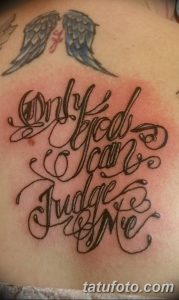 Фото тату надписи 'Only God Can Judge Me' с изображением крыльев на груди. Черно-коричневые тона, каллиграфический шрифт.
