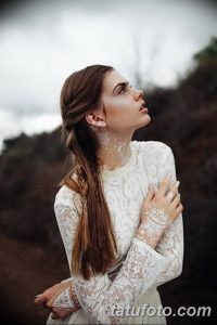 Фотография девушки с длинными каштановыми волосами, украшенной сложным белым узором на лице и плечах, выполненным в технике боди-арта.