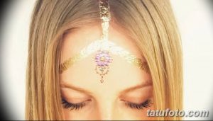 Фотография девушки со светлыми волосами, украшенной изящным золотым узором на лбу, выполненным в технике боди-арта.