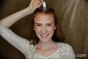 Фотография улыбающейся девушки с рыжими волосами, украшенной узором на бровях и волосах, выполненным в технике боди-арта.