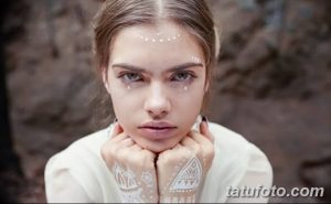 Фото тату: девушка с изящными белыми узорами на лице и руках, имитирующими временные татуировки, на фоне размытого леса.