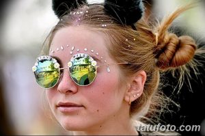 Фото тату: девушка в круглых солнцезащитных очках с надписью "Stay Wild" на очках и золотыми татуировками на лбу, демонстрирующая яркий и смелый образ.