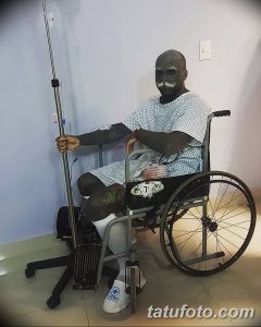 Фото пожилого мужчины с татуировками на лице, лежащего в больничной койке и подключенного к капельнице.