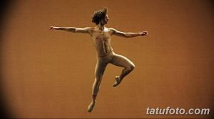 Фотография танцора в прыжке, демонстрирующая грацию и гибкость. Татуировки на теле танцора едва заметны, подчеркивая его атлетическое телосложение.