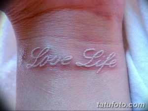 Фото белой татуировки на запястье: надпись "Love Life", выполненная каллиграфическим шрифтом, выглядит изящно и вдохновляюще.