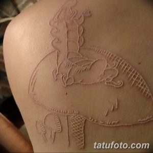 Фото белой татуировки дракона на спине. Изображение выполнено в технике white ink tattoo, с детальной проработкой чешуи и крыльев.