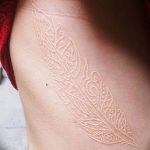 Фото белой татуировки в виде пера на боку. Нежный и изящный рисунок татуировки.