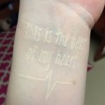 Фото тату на запястье: белая надпись 'This is the beat of my heart' и изображение кардиограммы. Необычный и стильный рисунок татуировки.