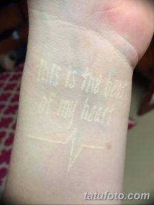 Фото тату на запястье: белая надпись 'This is the beat of my heart' и изображение кардиограммы. Необычный и стильный рисунок татуировки.