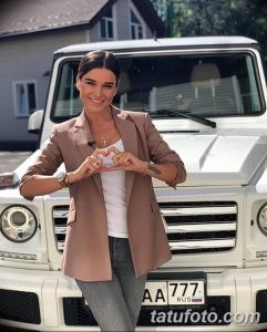 Фото татуировки на руке женщины на фоне автомобиля. Рисунок татуировки выполнен в темных тонах.