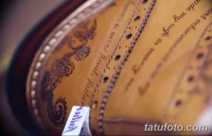 Крупный план татуировки на кожаном изделии, демонстрирующий сложные узоры и надписи, выполненные в коричневых тонах.
