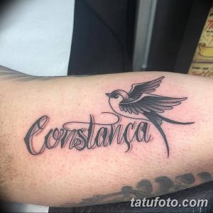 Фото татуировки на руке с надписью 'Constança' выполненной красивым шрифтом и изображением летящей ласточки.