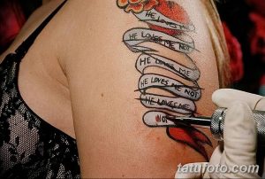 Фото татуировки с надписью "He loves me, he loves me not" (Он любит меня, он не любит меня), выполненной в виде цепочки из бумажных лент на плече.